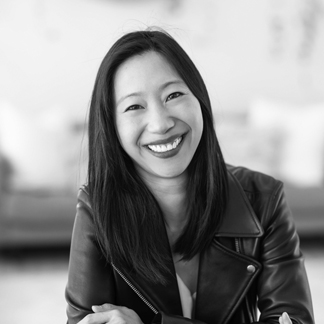 A monochrome headshot of Tiffany Yu smiling in a leather jacket.