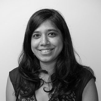 A monochrome headshot of Silky Shah, smiling broadly on a white background.